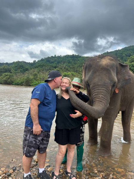 A couple kissing an elephant together at the riverside - lifeonwheel.com