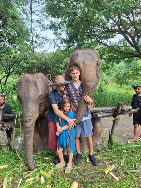 A family posing between two elephants reaching out with their trunks - lifeonwheel.com