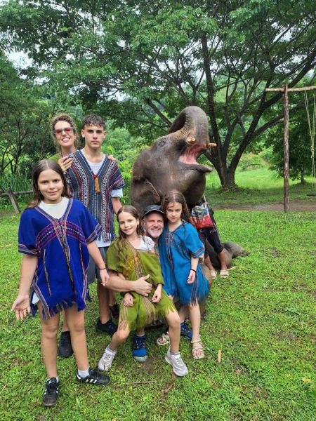 A family of six posing beside a playful elephant with its trunk raised - lifeonwheel.com