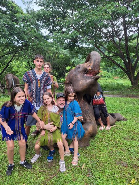 An elephant lying down as the family poses around it - lifeonwheel.com