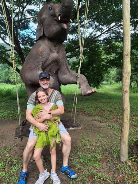 A father and daughter posing beneath an elephant standing on a rope swing - lifeonwheel.com