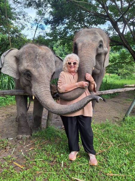 A grandmother embraced by the trunks of two elephants - lifeonwheel.com
