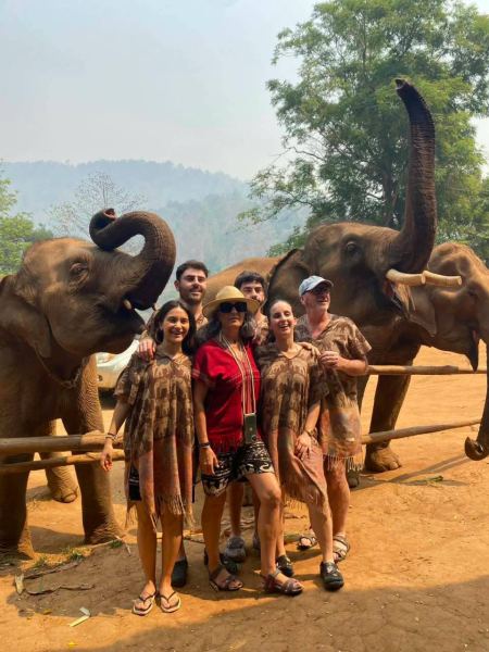 A group in matching outfits between two elephants with trunks raised, hazy hills behind - lifeonwheel.com