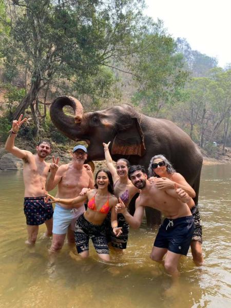 Friends cheering in a river next to an elephant with trunk curled up - lifeonwheel.com