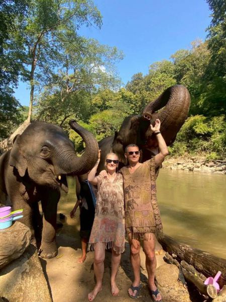 A couple raising their arms beside two elephants at the riverbank - lifeonwheel.com