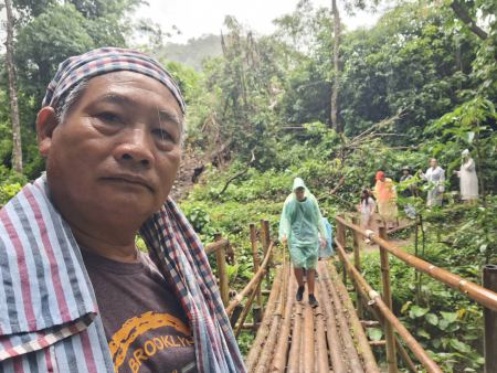 A close-up of the guide with trekkers crossing a bamboo bridge behind him - lifeonwheel.com